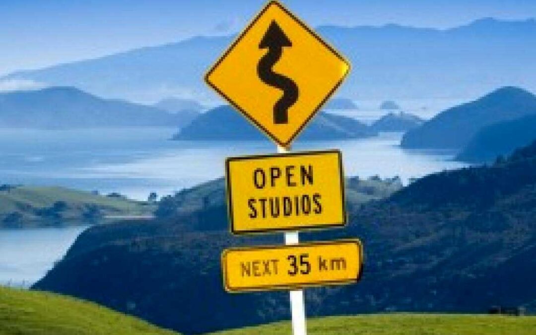 yellow traffic sign with squiggly arrow saying open studios next 35km in front of breathtaking view of ilsands and sea