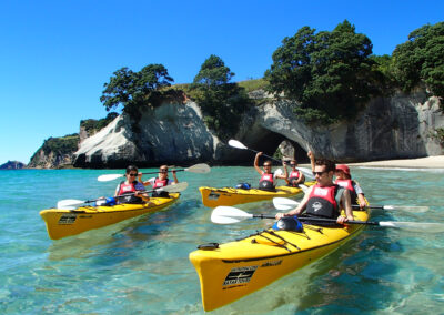 yellow kayaks with people floating on clear water in front of cliffs with trees